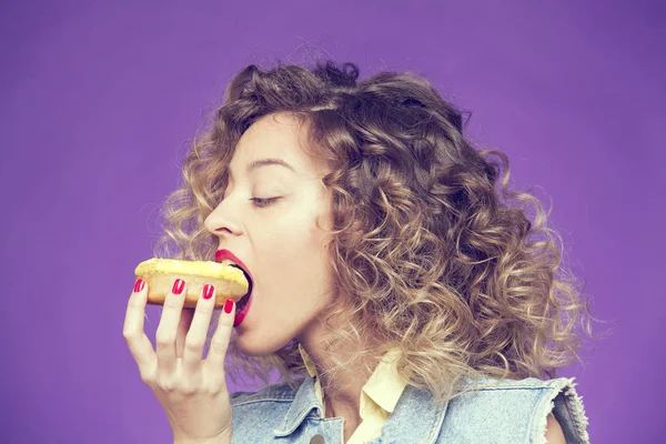 Kıvırcık kadın mor zemin üzerine lezzetli donut yemek