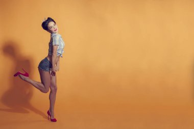 Sarı bir arka plan üzerinde pin-up tarzı genç kadın bacak şişiriyor