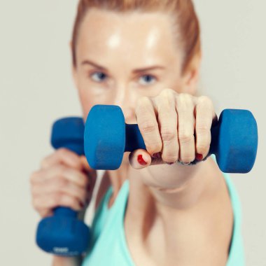 Yüzünün önünde dumbbells ile çalışan orta yaşlı kadın