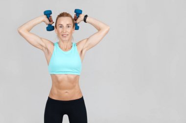 Orta yaşlı ince kadın elleri gri arka plan üzerinde dumbbells ile eğitim 