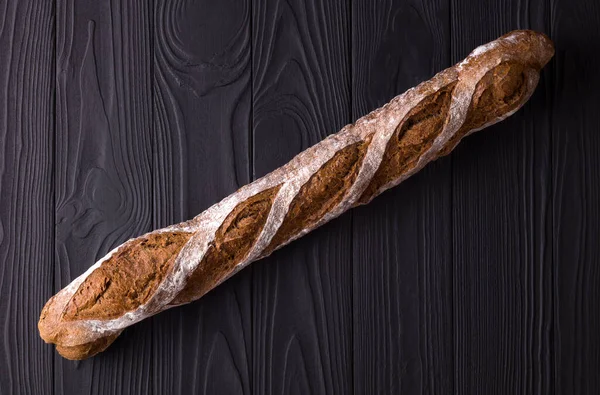 Top view photo of french rye baguette on black wooden table — ストック写真