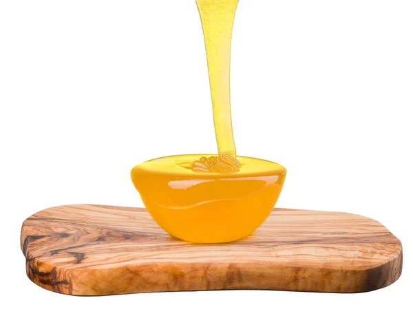 Glazen schaal vol honing en vallende straal honing op plank geïsoleerd op wit — Stockfoto