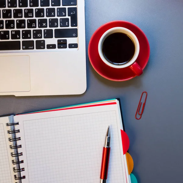 Workplace with laptop, notebook, coffee, pen, pin on desk.