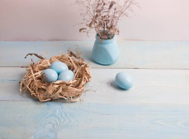 Mavi Paskalya yumurta yuvada ahşap arka plan üzerinde kuru ot ile vazo.
