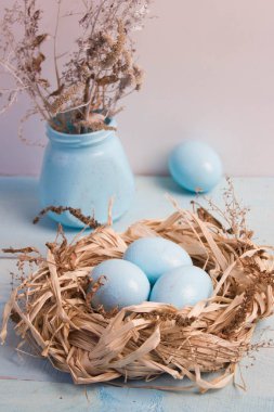 Mavi Paskalya yumurta yuvada ahşap arka plan üzerinde kuru ot ile vazo.