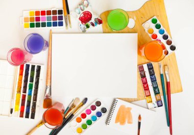 Boya ve fırçalarla çevrili boş kağıt sayfalarının üst görünümü