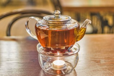 Cam çaydanlık masanın üstünde ve bir mum ile ısıtılıyor, doğal ışık, yakın çekim.