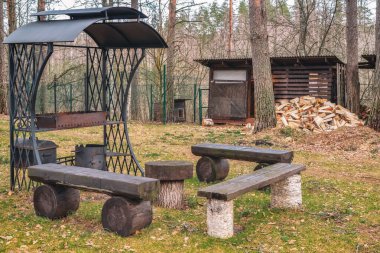 Ağaç ve ağaçların arka planında güzel bir deseni olan işlenmiş demirden yapılma antik metal brazier. Tablo ve kütüklerden yapılma banklar