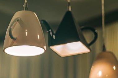 Ters çevrilmiş fincan şeklindeki kolye ışıkları ve bulanık arkaplanda çaydanlık.