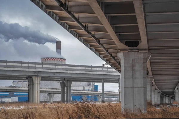 Çevre kirliliği. Çevresel bir sorun. Otoyol üst geçidi, viyadük 'ün altında. Güçlü beton sütunların ve büyük bir işletmenin sigara içme borularının manzarası. Kentleşme kavramı.