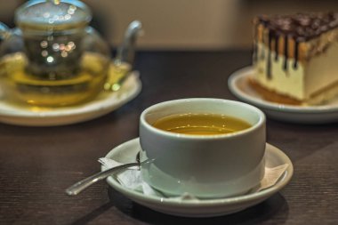 Şeffaf çaydanlık ve kekin bulanık arka planında bir fincan yeşil çay.