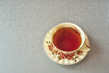 Gri masada çay fincanı var. Üzerinde gül resmi olan bir fincan çay. Doğal ışık