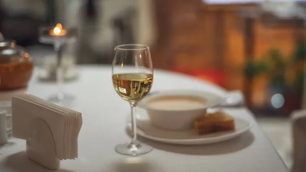 Restoranın arka planında masanın üzerinde bir bardak beyaz şarap var.