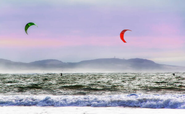 Kite surfers glide on the waves of the Atlantic ocean. Extreme sport concept. Active leisure landscape