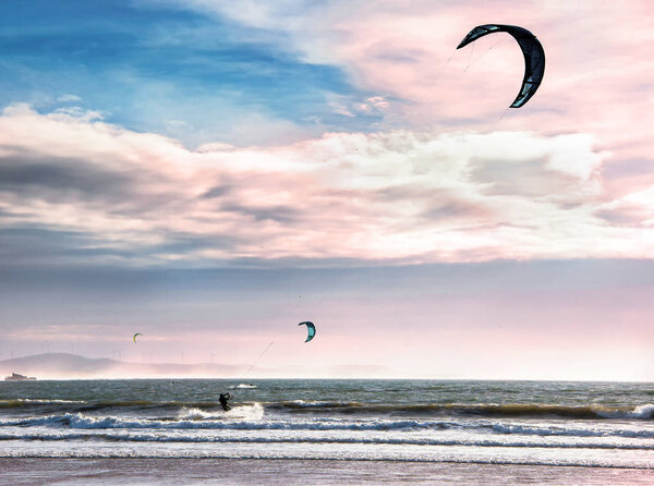 Kite surfers glide on the waves of the Atlantic ocean. Extreme sport concept. Active leisure landscape