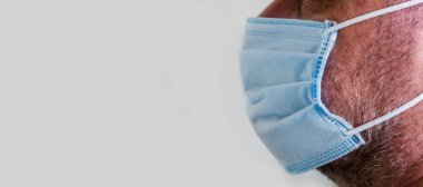 Mavi tıbbi koruyucu maskeli bir adam hafif arka planda izole edilmiş. Covid-19 Coronavirus Koruma Konsepti. Panoramik görüntü. Metnin için boşluk kopyala