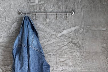 Eski alçı duvardaki askıda mavi kot ceket var. Moda giysiler.