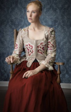 kızıl saçlı, 18. yüzyıl kadını işlemeli bir korse giyiyor.