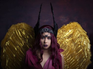 Güney Asyalı bir kadın savaşçı prenses gibi giyinmiş ve koyu kırmızı bir arkaplanda poz veriyor.