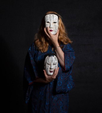 Çekici, kızıl saçlı, antika bir kimono giyen ve elinde iki klasik Japon maskesi tutan bir kadın.