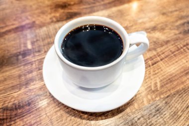 Bir fincan kahve ya da kopi. Kapalı bir yerdeki ahşap yapraklı masada oturuyorlar..