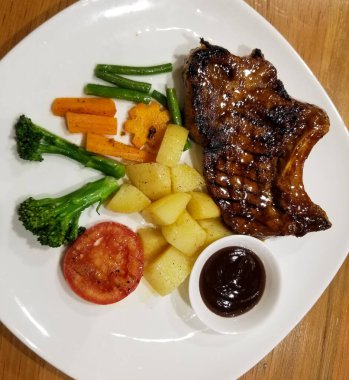 Beyaz tabakta bir tabak domuz pirzolası ve sebze..