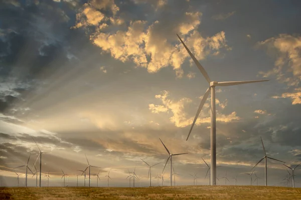 A field of Giant Wind Mill Generators in the Morning Light with the sunrays coming through the clouds in the sky.