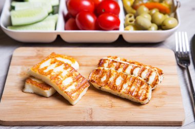 Grilled haloumi cheese on a wooden board with olives, cherry, cucumbers and pepperoni.  clipart