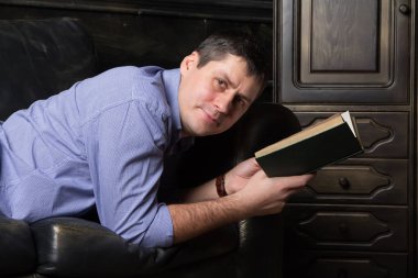 Genç adam kanepede yatıyor ve bir kitap okuyor. Yakın çekim.