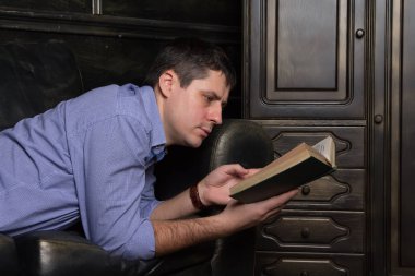 Genç adam kanepede yatıyor ve bir kitap okuyor. Yakın çekim.