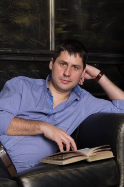 Genç adam kanepede yatıyor ve bir kitap okuyor. Yakın çekim.