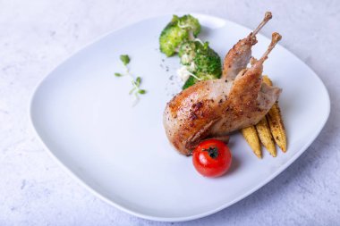 Brokoli, mini mısır ve vişneli domatesle kızartılmış bıldırcın. Beyaz plaka, hafif arka plan. Seçici odak, yakın plan.