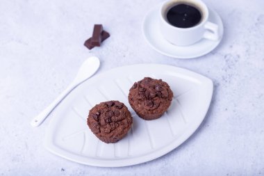 Beyaz tabakta çikolatalı kek. Ev yapımı pişirme. Arka planda bir fincan kahve var. Beyaz arka plan. Seçici odak, kapat.