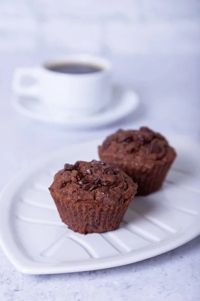 Chocolate muffins on a white plate. Homemade baking. In the background is a cup of coffee. White background. Selective focus, close up.