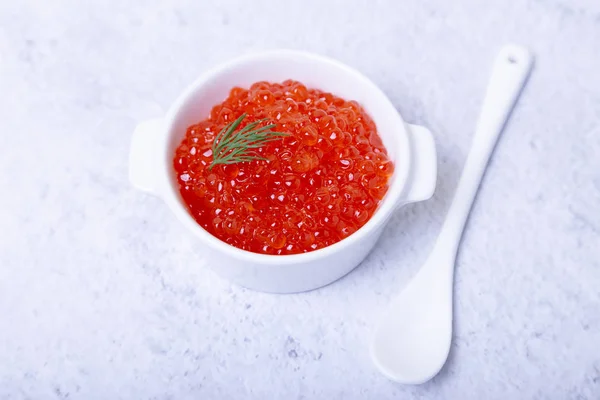 Red caviar (salmon caviar) in a white cup. White background, selective focus, close-up.