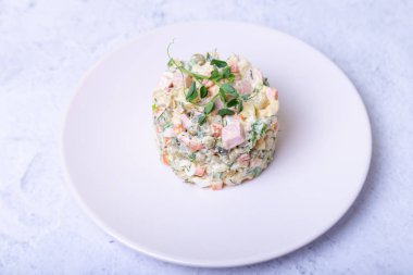 Beyaz bir tabakta bezelye filizleriyle süslenmiş Olivier salatası. Geleneksel Yeni Yıl ve Noel Rus salatası. Yakın çekim, seçici odaklanma.
