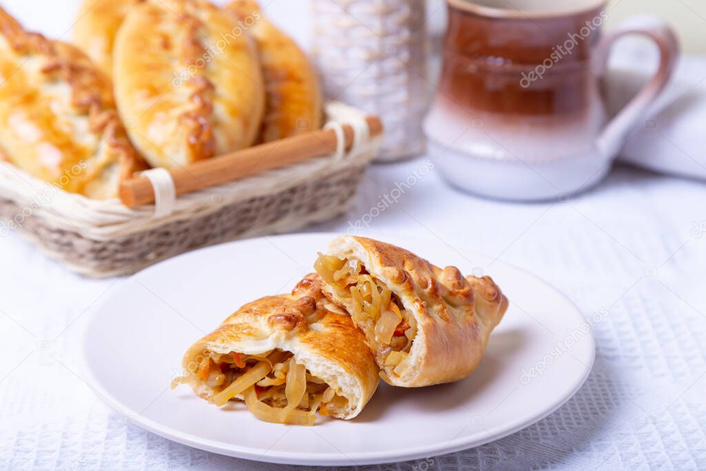 Pies (pirozhki) with cabbage. Homemade baking. Traditional Russian and Ukrainian cuisine. In the background is a basket with pies. Close-up.