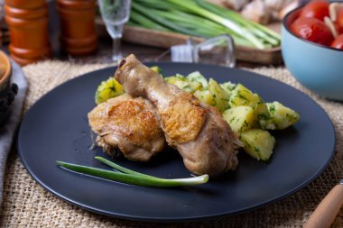 Patatesli tavuk, tuzlu domates ve mantar turşusu. Arka planda bir bardak votka, bir sürahi, bir tuzluk, soğan ve sarımsak var. Kırsal biçim.