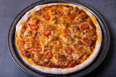 Somonlu pizza, domates ve kapari. Pizzanın tamamı siyah arka planda. Yakın plan..