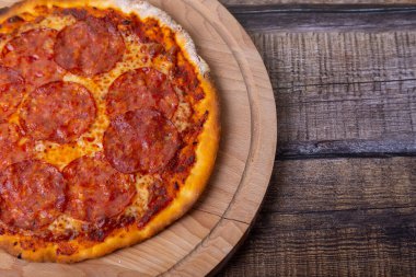 Tahta bir tahtanın üzerinde sucuklu pizza. Pizzanın tamamı. Yakın çekim, metin için yer.