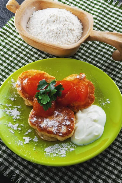 Pancakes with powder, cream and apricot jam on a plate. Wooden bowl with flour — Stock Photo, Image