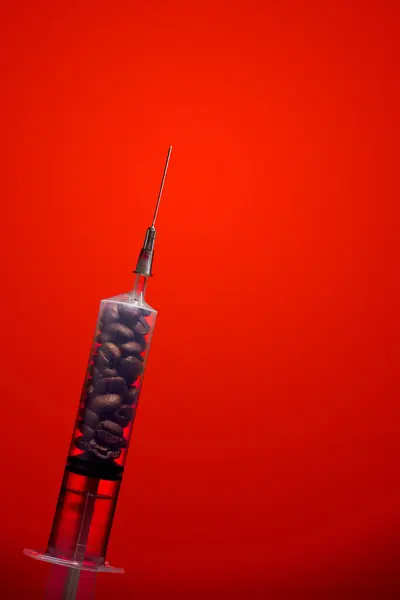 Kahve çekirdekleri içinde dramatik kırmızı bir arka plan üzerinde bir şırınga. Kafein bağımlılığı