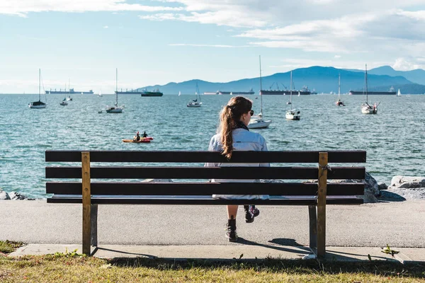 Meisje zittend op een bankje op het strand van Kitsilano in Vancouver, Canada — Stockfoto