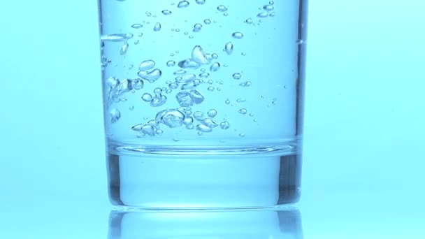 Glas sprudelndes Wasser vor blauem Hintergrund, Zeitlupe — Stockvideo