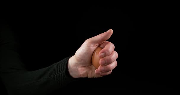 Mano del hombre rompiendo un huevo de pollo contra fondo negro, cámara lenta 4K — Vídeo de stock