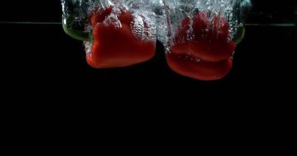 Красный перец, капсик однолетний, вегетарианский, падающий в воду на черном фоне, медленное движение 4K — стоковое видео