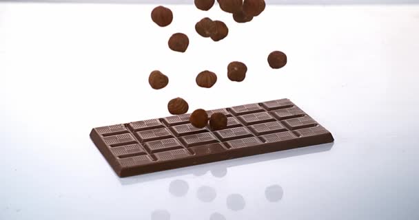 Hazelnuts falling on Milk Chocolate tablet — Stock Video