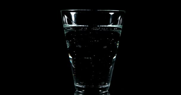 Bruisend Water in een glas tegen zwarte achtergrond, realtime 4k — Stockvideo