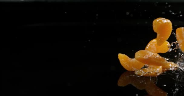 Клементина, цитрусовые сетчатки, фрукты падают на воду на черном фоне, медленное движение 4K — стоковое видео