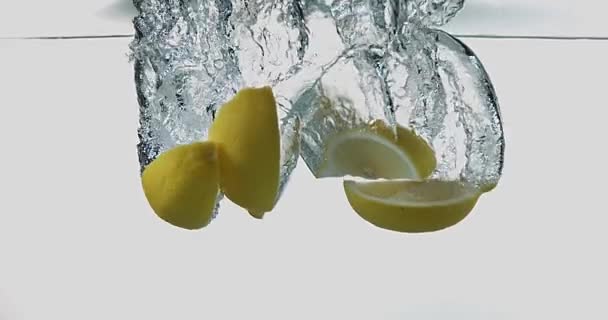 Limones amarillos, limonum cítrico, Frutas que caen al agua contra el fondo blanco, cámara lenta 4K — Vídeo de stock